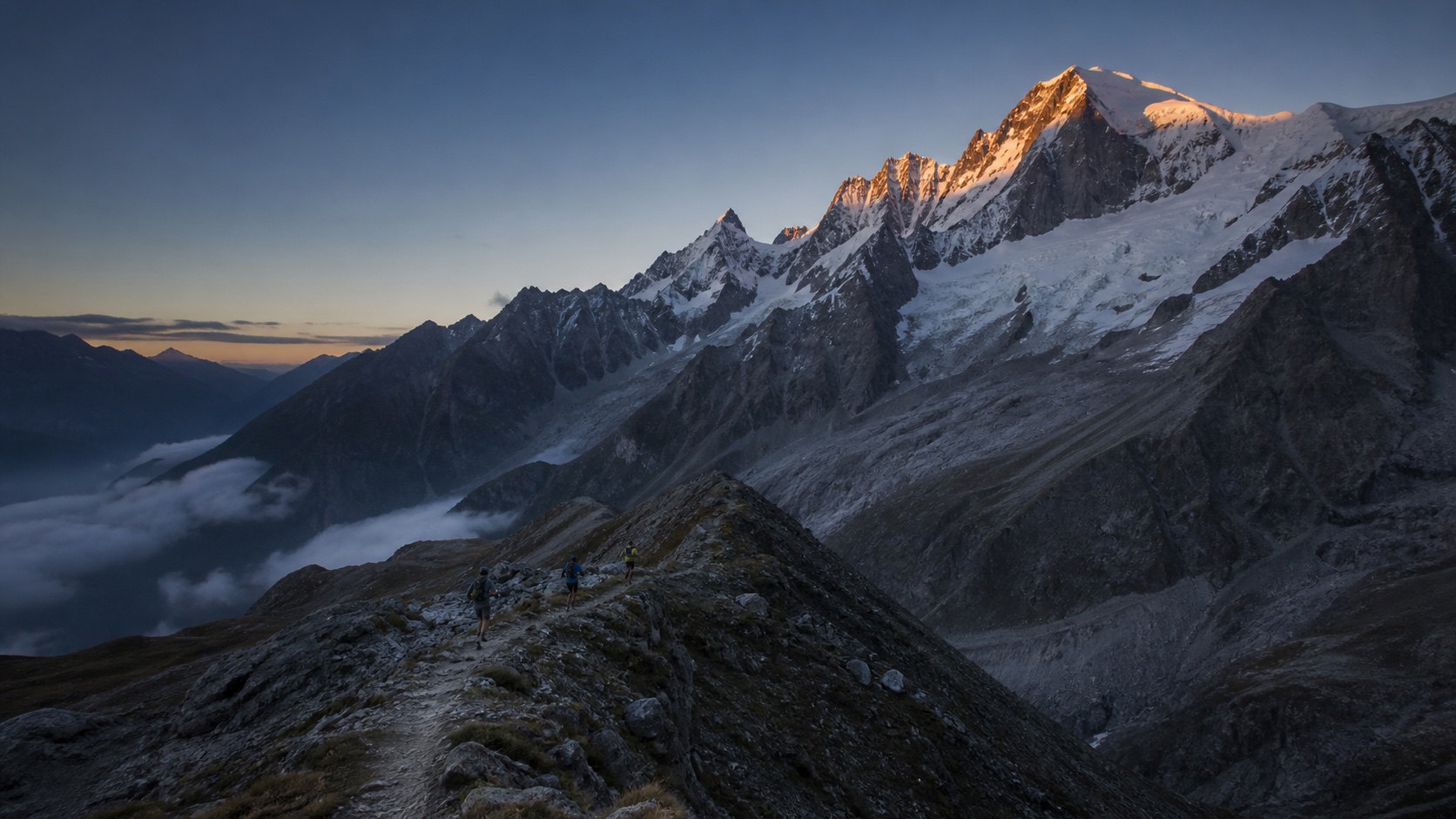 Trail runners crossing a high Alpine ridge at first light